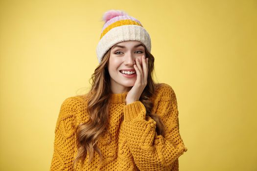 Smiling attractive carefree young 20s woman having fun talking casually nice conversation girlfriend press palm cheek amused blushing receive flirty compliment, standing positive yellow background.