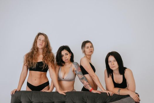 Diverse models wearing comfortable underwear posing on a large sofa, look at camera having smile and natural unique beauty