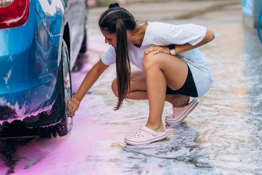 Brunette with two pigtails with a sponge washes the rim of a car