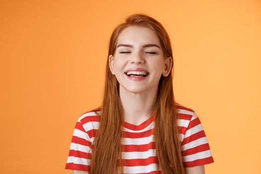 Sincere happy charismatic redhead girl smiling, close eyes enjoy warm summer sunbeams, laughing cheerful, feel relaxed rejoicing, show white teeth, good vacation concept, orange background.