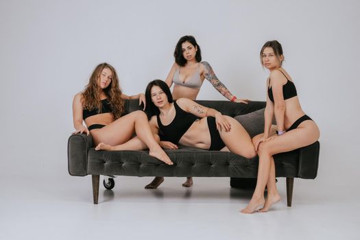 Diverse models wearing comfortable underwear posing on a large sofa, look at camera having smile and natural unique beauty