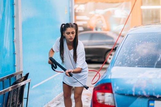 Brunette with two pigtails from a high-pressure hose washes the car at a car wash