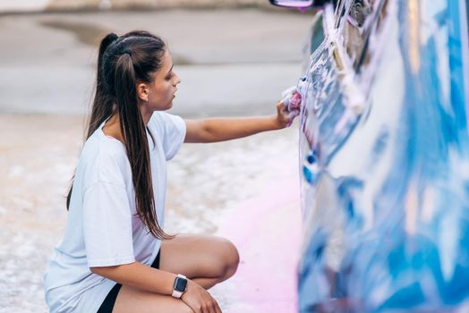 Woman with two pigtails with a sponge washes the side of the car