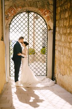 Groom kisses bride on the forehead near the decorative gate in the courtyard. High quality photo