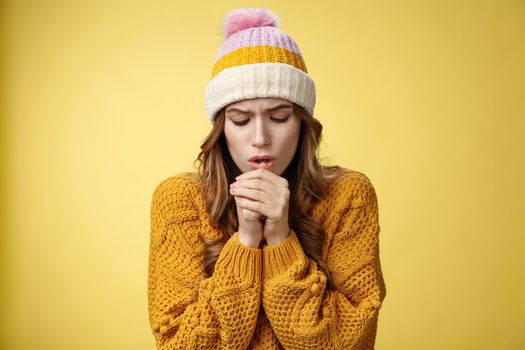 Close-up upset uncomfortable cute tender young caucasian woman breathing warm air hands warm-up freezing-cold outside stooping trembling wearing light clothes, standing yellow background.