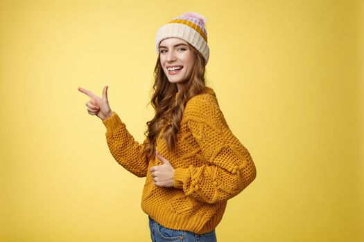 Profile shot charismatic flirty good-looking satisfied young girl turn camera pointing index finger left show thumbs-up like gesture approving recommending awesome place yellow background.