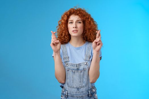 Impatient worried hopeful pretty ginger girl curly hairstyle squinting intense stare praying cross fingers good luck awaiting important news willing wish come true achieve desire dream fulfill.