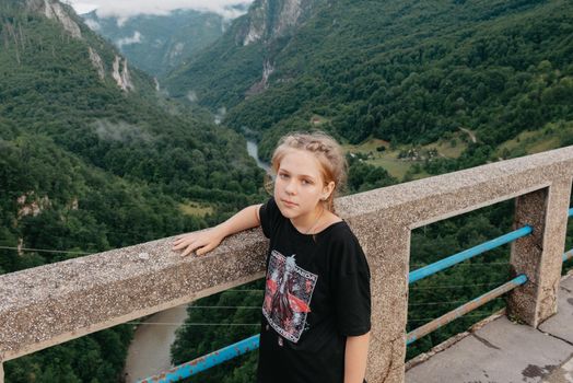 A girl stands on a bridge with a beautiful view of the mountain landscape