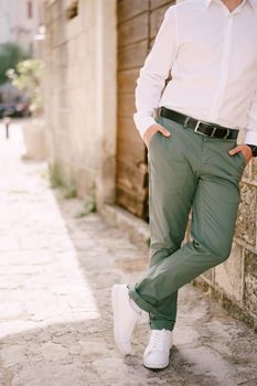 Man in green trousers and a white shirt is leaning against the wall of a stone house. Close-up. High quality photo