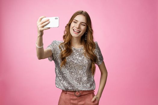 Sociable good-looking confident feminine caucasian woman recording video message taking selfie holding smartphone upper angle capturing image partying send photo online, posing pink background.