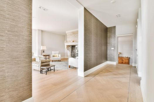 A wide corridor covered with brown wallpaper and an arch leading to the living room