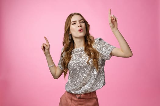 Girl dancing celebrating birthday party having fun carefree folding lips satisfied moving music rhythm pointing fingers up joyfully standing happy pleased pink background, wearing glamour blouse.