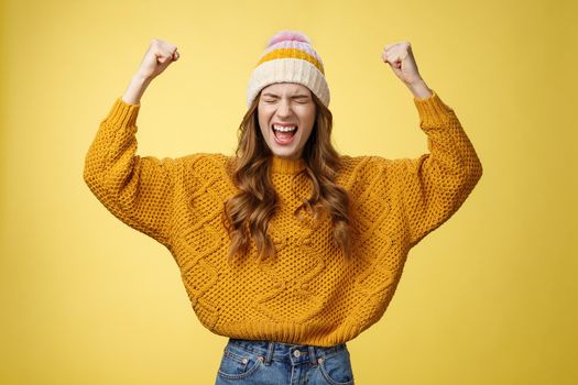Relieved attractive fashionable university female student yelling proudly raise clenched fists victory cheer gesture celebrating win successful achievement accomplishment goal, yellow background.