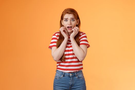 Innocent scared redhead female victim feel afraid standing stupor trembling fear, drop jaw gasping shocked, stare terrified, speechless look camera, frightened stand orange background.