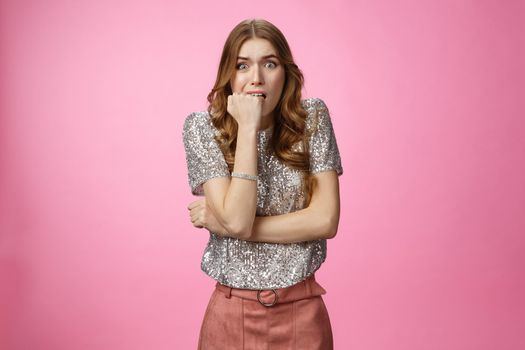 Worried insecure cute glamour caucasian woman biting fist nervously widen eyes scared bad consequences, frightened afraid parents find out, standing shocked stupor pink background.