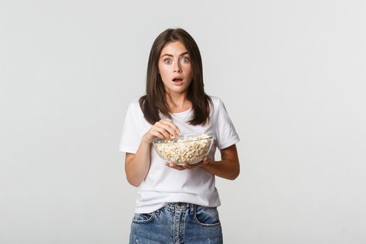 Portrait of thrilled and amazed young woman eating popcorn and watching movies or tv series.