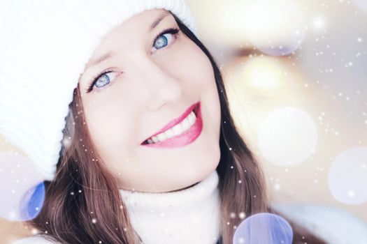 Christmas, people and winter holiday concept. Happy smiling woman wearing white knitted hat as closeup face xmas portrait, snow glitter and bokeh effect.