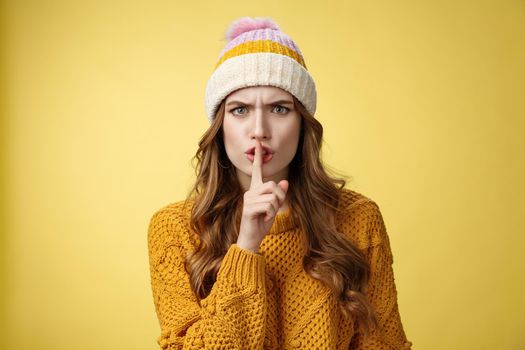 Furious angry annoyed cute woman shushing you irritated loud talk during important meeting frowning cringing pissed showing shhh gesture index finger pressed mouth, yellow background.