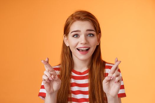 Excited hopeful redhead girl hope win lottery, smiling optimistic, look faith, believe dream come true, cross fingers good luck, make wish, anticipate good news, praying fortune, orange background.
