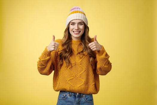 Supportive attractive 20s girl likes your idea show thumbs up positive reply affirmative answer standing pleased smiling recommending promotion satisfied give approval, agree yellow background.