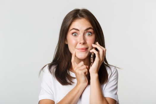 Close-up of intrigued smiling girl talking on smartphone with tempted expression.