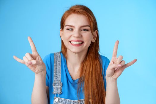 Close-up cheerful lucky joyful redhead woman having fun, enjoying summertime, show rock-n-roll gesture attend awesome party concert, make heavy-metal sign and smiling blue background.