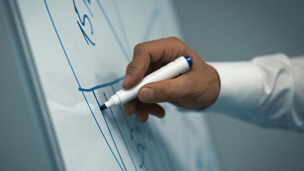 Businessman draws round diagram, pie chart with marker on white board. Close up shot of male hand. Toned image.