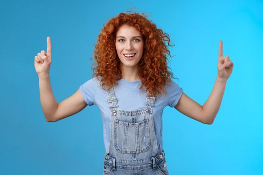 Energized enthusiastic good-looking redhead cheerful curly girl pointing up index fingers motivated present awesome copy space smiling delighted glad summer warm days near beach blue background.