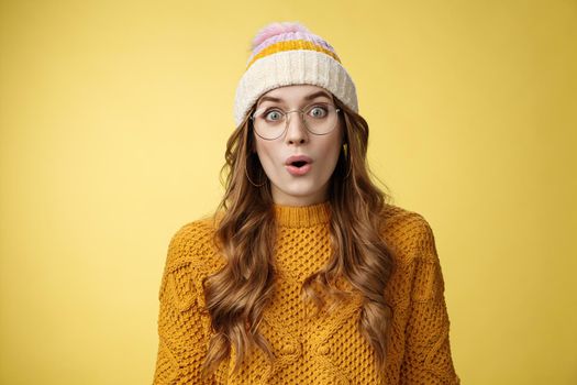 Surprised amazed charismatic good-looking young female student widen eyes wondered say wow amazed standing shocked impressed yellow background, wearing nerd glasses hat sweater.