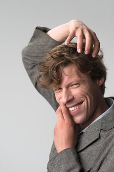 Young handsome man smiling positively and confidently posing with hands on his face and head, looking satisfied, friendly and happy against grey background. Facial expressions, emotions, feelings.