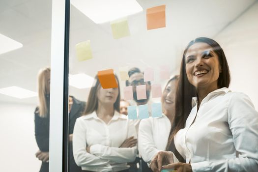 Group of young business people use multi-colored sticker papers posting them on the glass wall working on ideas and communicating together in the creative office. A successful team concept.