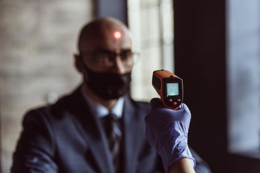 Health officer checking temperature of a businessman in the entrance of the business center. Businessman must go through fever measures using infrared digital thermometer check, Covid 19 concept.