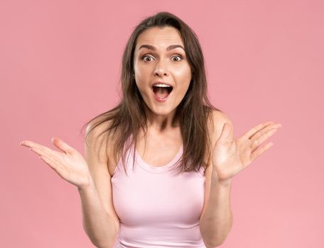 Charming acting surprised girl wearing pink t-shirt with hands in the air, excited and joy expression on her face with positive emotions. Facial expressions, emotions, feelings.