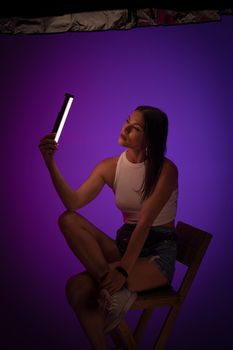 Woman holds LED lamp looking on it against of purple background. Presentation of Nanlite Studio Lighting. Backstage concept. June 2020, Kiev Ukraine.