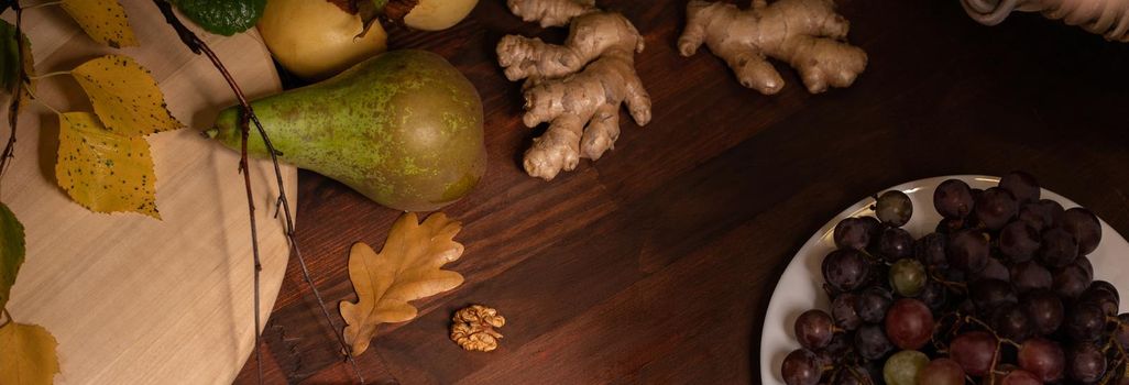 Panoramic banner. Close up top view of a fruits, grapes, ginger root on a wooden table. Wine snacks set: selection of cheese, grapes, pear and walnuts on a wooden board.
