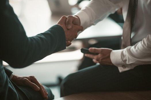 Two businessmen handshaking colleagues or business partners on modern office background. Business concept. Close up shot.