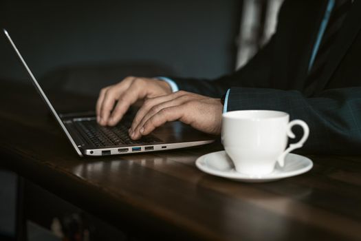 Close up professional businessman working on laptop and drinking cup of coffee sitting at the modern office. Man working on laptop in office. Business and finance concept.