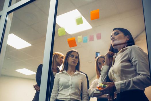 Young professional team. Group of young freelancers use sticker papers posting on the glass wall working on ideas and communicating together in the creative office. Successful team concept.