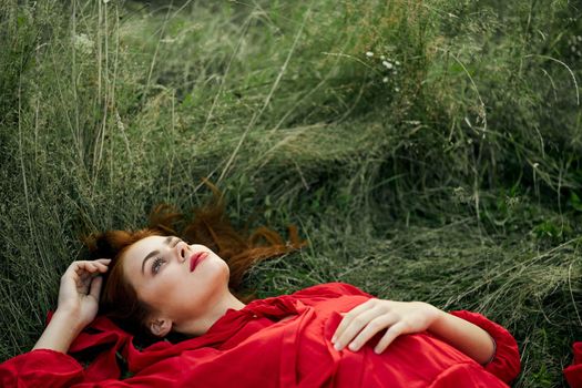 pretty woman in red dress lies on the grass freedom landscape. High quality photo