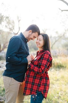 Smiling man holding hands of pregnant woman touching his forehead to her forehead. High quality photo