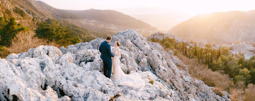 Bride and groom hug on the rocks against the background of mountains. High quality photo