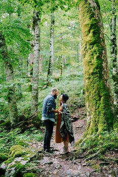 Pregnant woman with a man stands on a path in a green park, holding hands. High quality photo