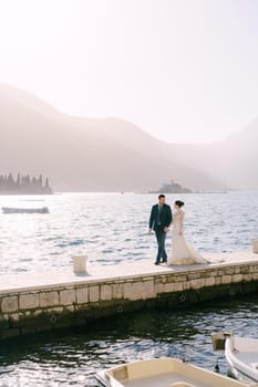 Bride and groom walk along the pier against the backdrop of the islands near Perast. Montenegro. High quality photo