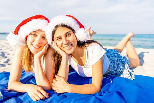 Couple of lying on the beach looking at camera wearing Santa Claus hat. Two young women having fun in ocean sea holidays vacations taking a self-portrait at the tropical beach