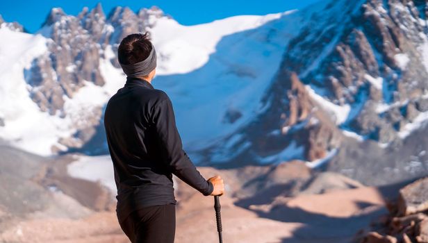A young man travels, goes to the mountains in thermal underwear and with trekking poles, a hiker climbs to the top of the mountain, against the backdrop of red rocks and a glacier.