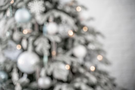 Close-up of a festively decorated outdoor Christmas tree with balls on a blurred sparkling fairy background. Defocused garland lights, bokeh effect