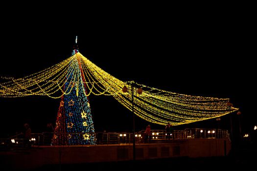 Long exposure night shot of a uniquely decorated main Christmas tree in the square after rain with reflection