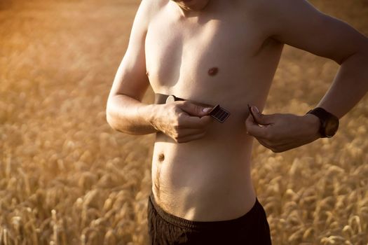 A young male athlete puts on a heart rate monitor and smart watch before jogging in nature. A man monitors his pulse and is engaged in a healthy running at sunset.