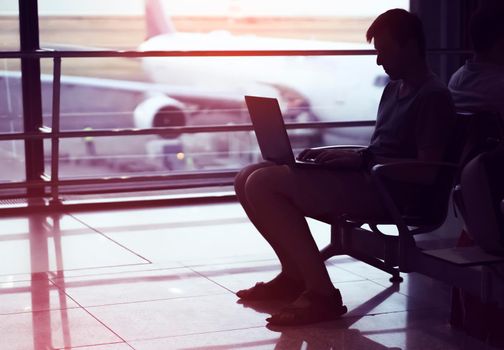 A young man is working on a laptop at the airport while waiting to board the plane. A man is engaged in business, buys tickets, studies and communicates via the Internet in the evening.