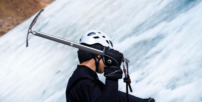 A young man traveler uses an ice ax while hiking in the mountains, a hiker with climbing equipment, in a helmet, crampons climbs to the top of a snow-capped mountain.